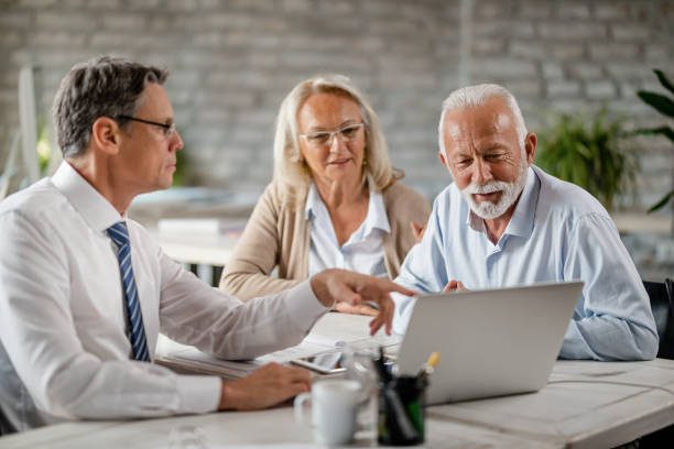deal old Senior couple using laptop with their financial advisor during a meeting int he office. Focus is on senior man.